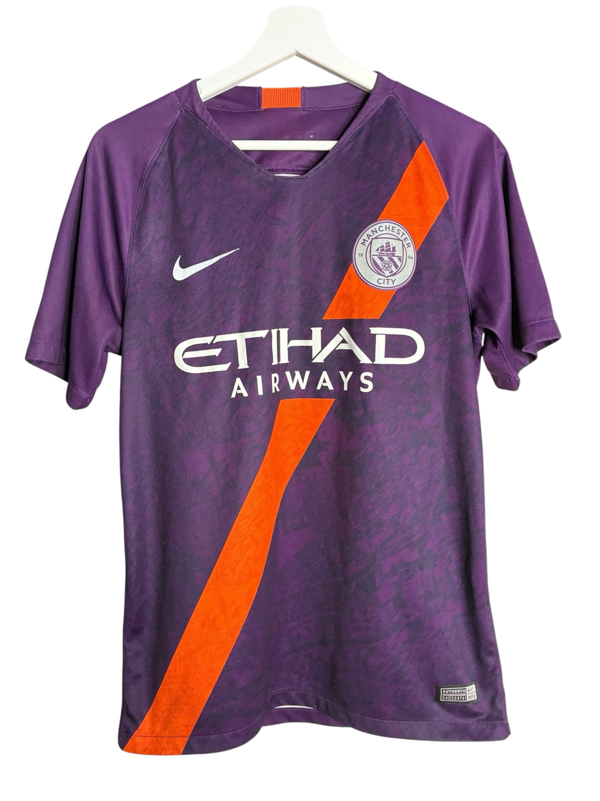 Maillot de football Nike Manchester City violet avec bande diagonale orange, disponible chez Levestiairedupeuple.
